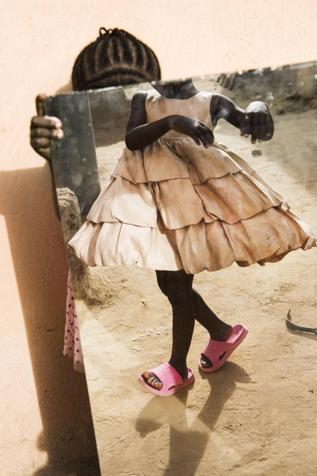 Một bé gái giơ tấm gương kính để người chị gái mình soi vào và thử chiếc váy mới tại sân chơi của trại trẻ mồ côi ở Gwagwalada, gần thủ đô Abuja của Nigeria.