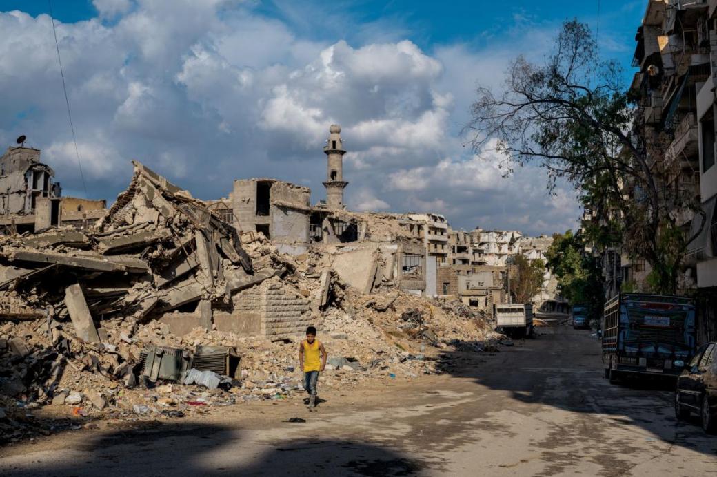 Một cậu bé bước đi trước một ngôi trường và Nhà thờ Hồi Giáo ở khu phố Sukkari, phía nam thành phố Aleppo. Ngôi thánh đường đang được xây cất lại trong khi những tòa nhà xung quanh vẫn còn trong tình trạng đổ nát.