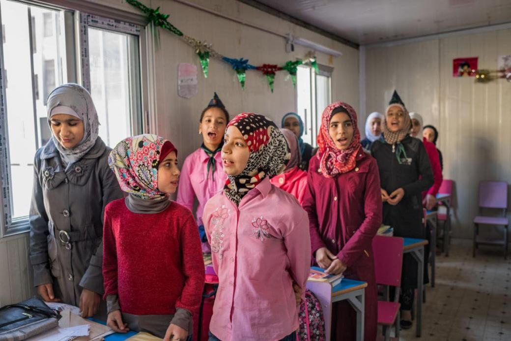 Những nữ sinh cùng nhau hát trong tiết học đầu tiên của ngày tại trường học Ibn al Nafees, phía đông khu Al Myassar của thành phố Aleppo. Ngôi trường này đã có 15.000 học sinh và 6 tòa nhà khi nó đóng cửa vào 5 năm trước. Mở cửa lại với 1.000 học sinh vào tháng 10 vừa qua, phòng học bây giờ là những căn phòng đúc sẵn, kém tiện nghi hơn nhiều so với những tòa nhà hiện đại đã bị hư hỏng nặng.