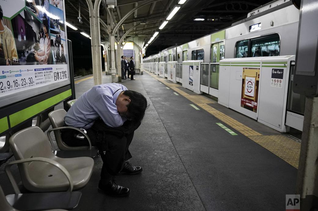 Nhân viên công sở ngồi gục xuống đùi để chợp mắt nghỉ ngơi trong khi đợi chuyến tàu đưa anh đến công ty.