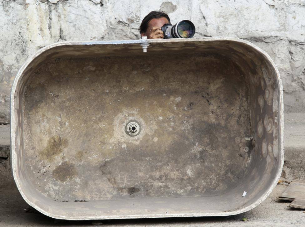 a photographer takes his position behind an empty water tank during an operation at alemao slum in rio de janeiro november 27 2010