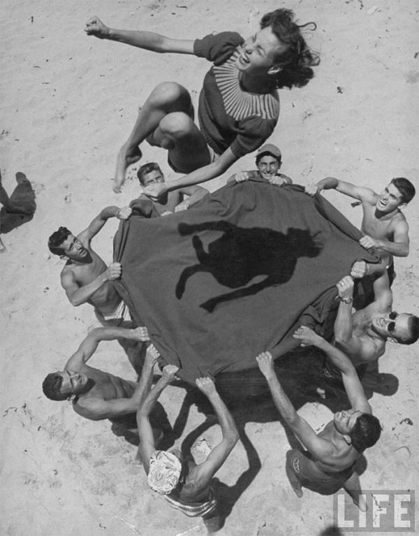 teenaged boys using blanket to toss their friend norma baker into the air on the beach 1948