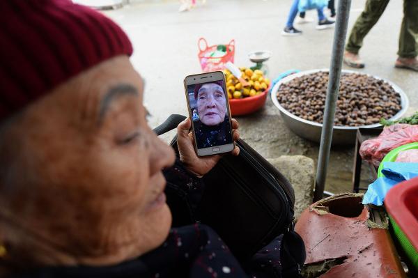 Ngo Thi Pho (75 tuổi), đang sử dụng điện thoại của bà để giải trí, trong lúc đợi khách tại sạp hàng của mình ở một khu chợ ven đường tại tỉnh Hà Giang, miền bắc Việt Nam. Ảnh: Nhac Nguyen/AFP/Getty.