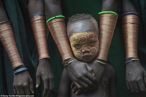 7377444 6491533 a young boy stands among suri women wearing copper bracelets in a 82 1544703332533