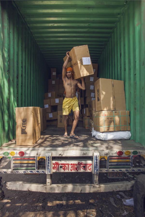 Ở kho xe tải Bhiwandi tại Mumbai, một chiếc xe tải chở đầy hàng hóa không nhãn mác được chuyển đến từ Delhi đang được các cửu vạn dỡ đi nhanh chóng và đưa đến các thương lái đang chờ sẵn.