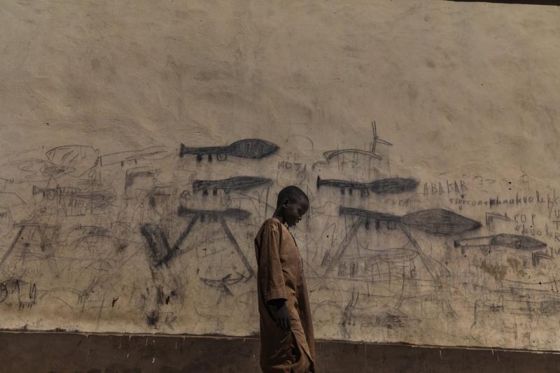 Một cậu bé mồ côi đi ngang qua bức tường vẽ cảnh súng bắn lựu đạn và tên lửa chiến tranh ở Bol, Chad. Ảnh: Marco Gualazzini.