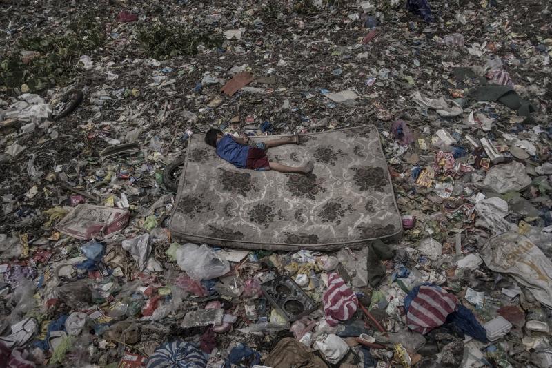 Một cậu bé hành nghề thu gom phế liệu đang ngủ trên một tấm nệm bỏ đi quanh bãi rác nổi trên sông Pasig ở Manila, Philippines. Con sông này đã chết về mặt sinh học từ những năm 1990 vì lượng chất thải lớn được đổ trực tiếp vào đây từ các nhà máy lẫn những hộ dân cư mà không qua xử lý. Sông Pasig ‘đón nhận’ 63.700 tấn rác thải nhựa mỗi năm, chất thải dày đến mức có thể đi bộ trên mặt sông, rác tạo thành những hòn đảo nhân tạo nổi lềnh bềnh. Ảnh: Mário Cruz.
