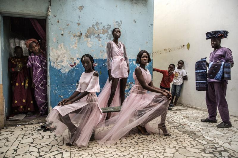 Diarra Ndiaye, Ndeye Fatou Mbaye và Mariza Sakho đang mặc những bộ trang phục của nhà thiết kế Adama Paris trong khu phố cổ Medina ở thủ đô Dakar của Senar trước sự tò mò của những người xung quanh. Dakar là trung tâm phát triển của dòng thời trang Pháp-Phi và là nơi đặt kênh Fashion TV Châu Phi, kênh truyền hình về thời trang đầu tiên ở châu lục này. Ảnh: Finbarr O'Reilly.