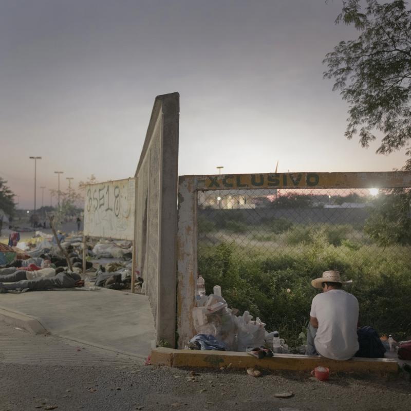 Bình minh đang đến tại một trạm xe buýt ở Juchitán, Mexico, bên cạnh đó là những người di cư đang nằm ngủ trải dài trên vỉa hè trong cảnh màn trời chiếu đất.